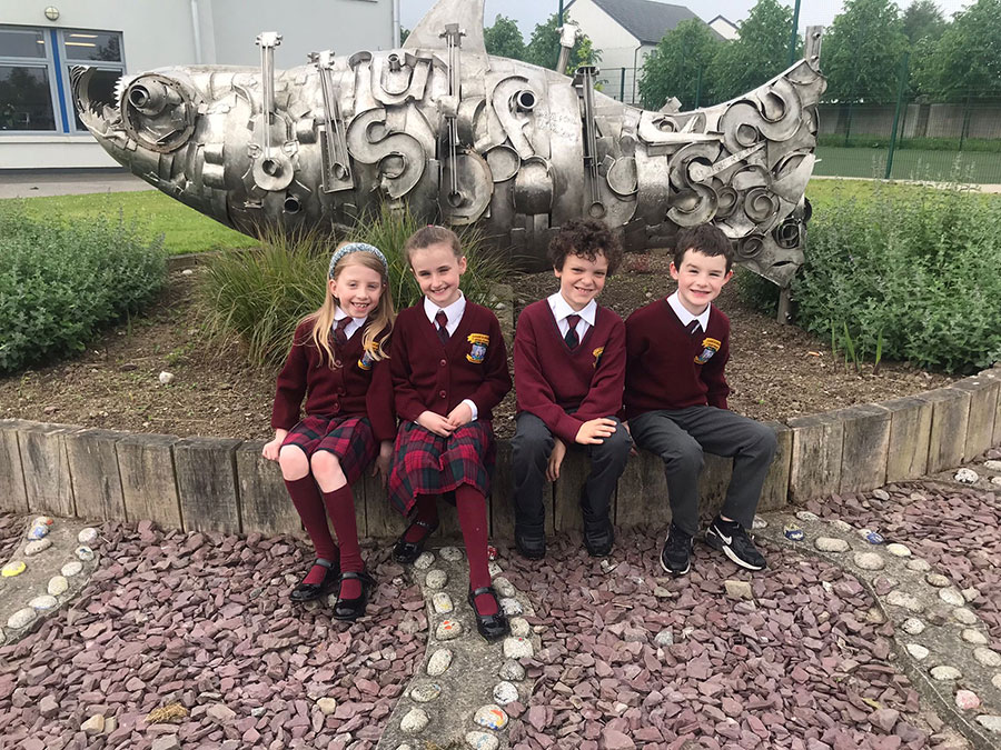 Children wearing the Gaelscoil Uí Fhiaich school uniform by the fist scultpure