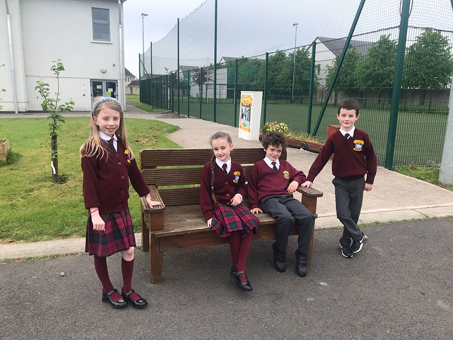 Children wearing the Gaelscoil Uí Fhiaich school uniform by a year bench